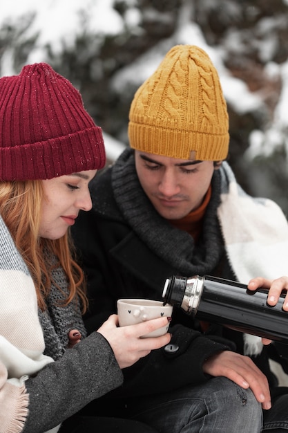 Photo gratuite vue de face couple avec des vêtements d'hiver verser des boissons chaudes