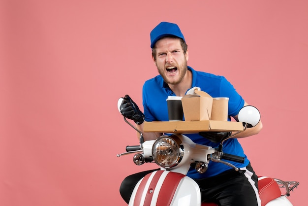 Vue de face courrier masculin en uniforme bleu tenant une boîte de café et de nourriture sur un service de couleur de vélo de travail de livraison de restauration rapide rose