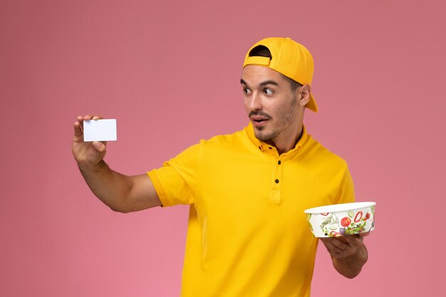 Vue de face de courrier masculin en uniforme jaune tenant le bol de livraison avec carte sur le fond rose.