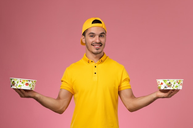 Vue de face de courrier masculin en uniforme jaune tenant des bols de livraison sur le fond rose.