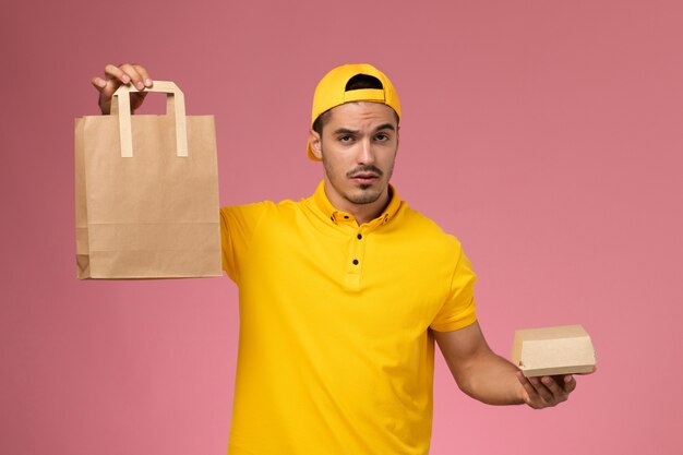 Vue de face de courrier masculin en uniforme jaune tenant des colis alimentaires de livraison sur fond rose.