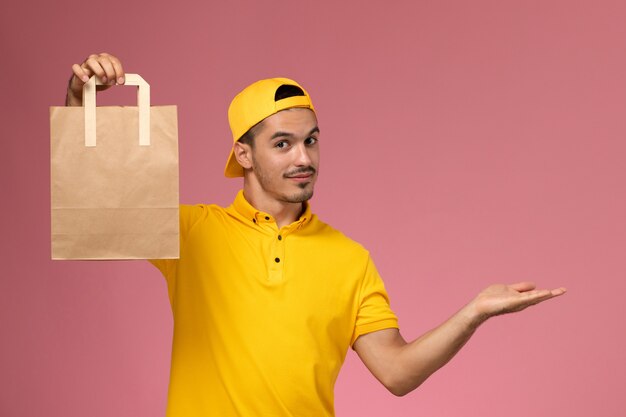 Vue de face de courrier masculin en uniforme jaune tenant le paquet de papier de livraison sur fond rose clair.