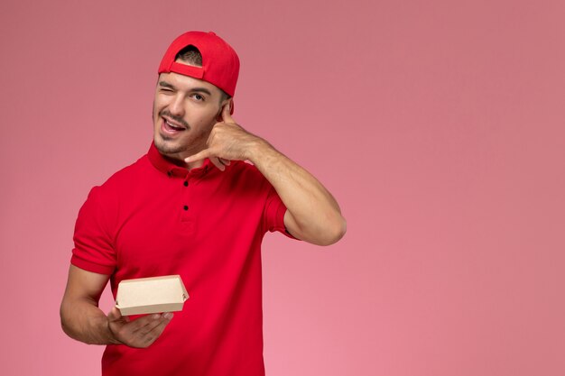 Vue de face de courrier masculin en uniforme rouge et cape tenant peu de colis de livraison clignotant sur fond rose.