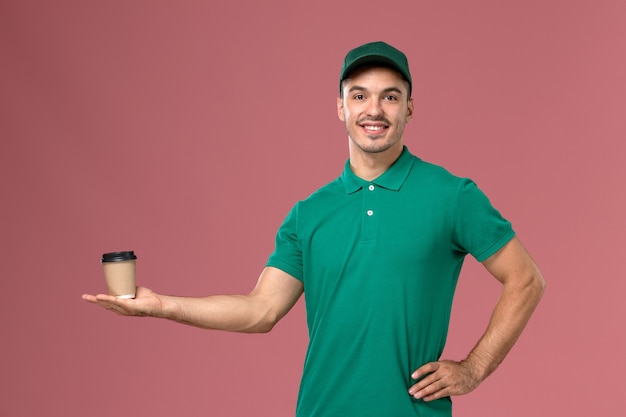 Vue De Face De Courrier Masculin En Uniforme Vert Souriant Et Tenant Une Tasse De Café Sur Le Fond Rose