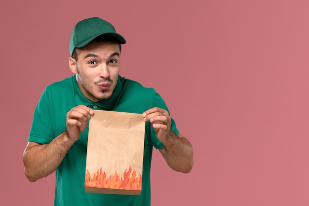 Vue de face de courrier masculin en uniforme vert tenant un paquet de papier alimentaire sur le fond rose clair