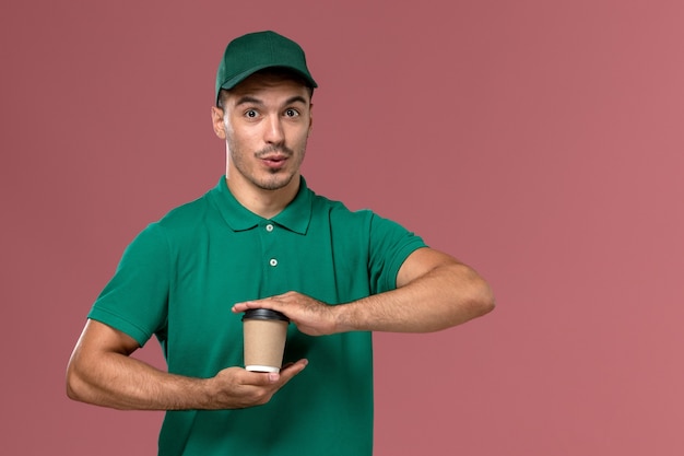 Vue de face de courrier masculin en uniforme vert tenant la tasse de café de livraison sur le fond rose clair