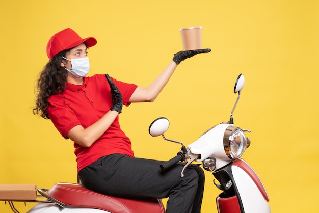 Photo gratuite vue de face coursier féminin dans un masque tenant un dessert de livraison sur fond jaune covid- travail uniforme de travail livraison de travail