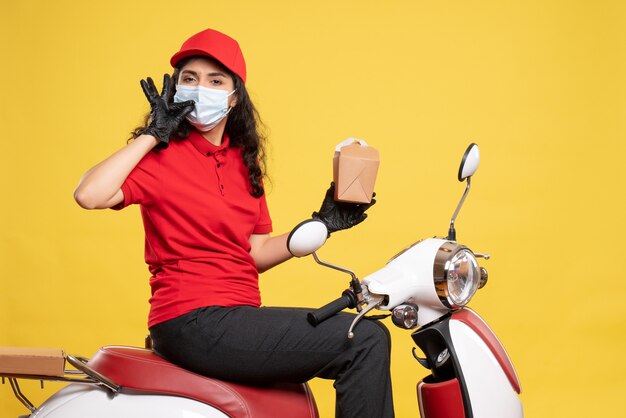 Vue de face coursier féminin en masque avec petit paquet de nourriture sur le service de bureau jaune uniforme de travailleur pandémique covid-livraison de travail