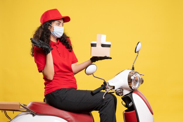 Vue de face coursier féminin en masque avec des tasses à café sur fond jaune service covid-travailleur uniforme de travail