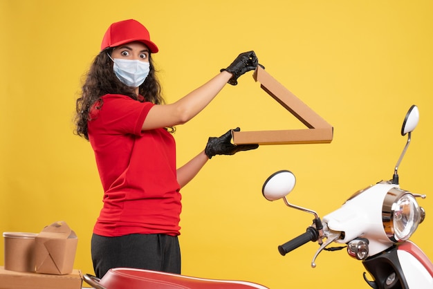Vue de face coursier féminin en uniforme rouge avec boîte à pizza sur fond jaune livraison de travailleur covid- travail de virus de service pandémique