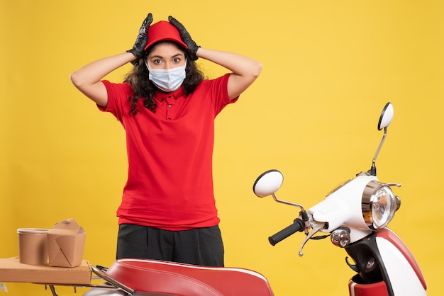 Vue de face coursier féminin en uniforme rouge et masque sur fond jaune covid - prestation de service d'emploi uniforme travailleur pandémie