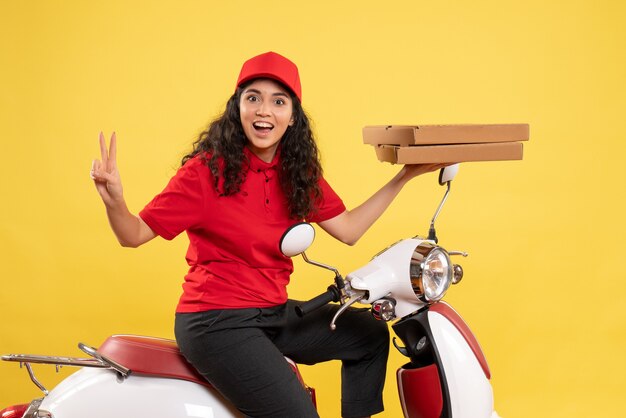 Vue de face coursier féminin sur vélo tenant des boîtes à pizza sur fond jaune service d'emploi travailleur uniforme femme livraison travail