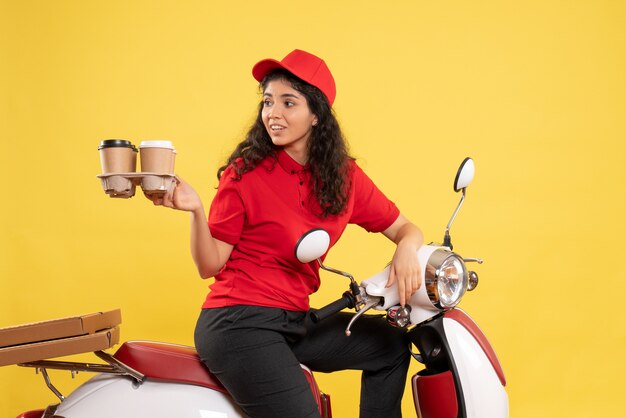 Vue de face coursier féminin sur vélo tenant des tasses à café sur fond jaune travail de service de travailleur femme travail de livraison
