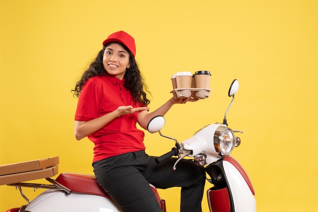 Vue de face coursier féminin sur vélo tenant des tasses à café sur fond jaune travail uniforme de service de travailleur travail de livraison de femme