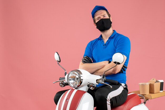 Vue de face coursier masculin en uniforme bleu et masque sur le travail de livraison de travail de vélo de virus rose travail de restauration rapide