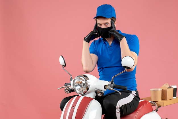 Vue de face coursier masculin en uniforme bleu et masque sur un travail de livraison de travail à vélo à virus rose travail de service de restauration rapide covid