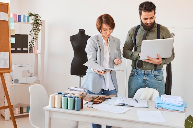 Vue de face des créateurs de mode travaillant en atelier avec ordinateur portable