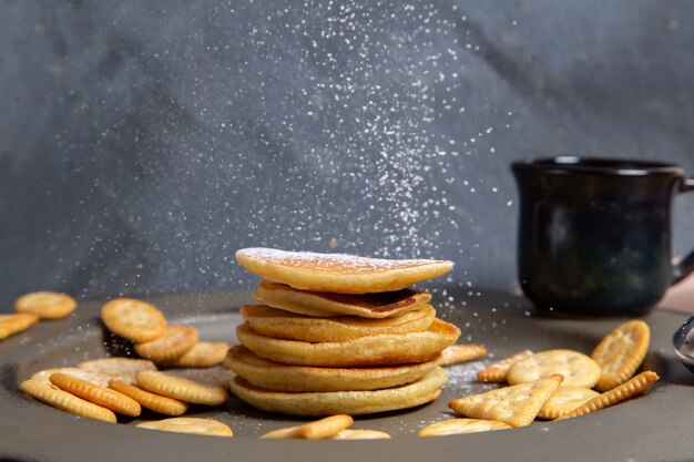 Vue de face crêpes et craquelins avec tasse de lait noir sur fond gris