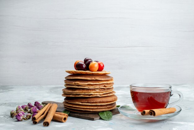 Une vue de face des crêpes rondes cuites au four et délicieuses avec du thé aux cerises sur le gâteau de bureau léger aux fruits