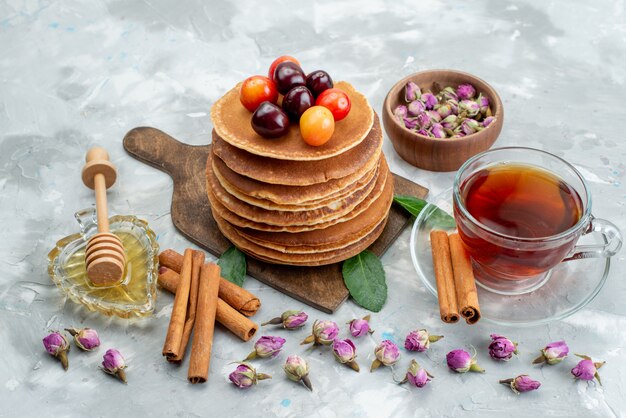 Une vue de face des crêpes rondes cuites au four et délicieuses avec du thé aux cerises sur le gâteau de bureau léger