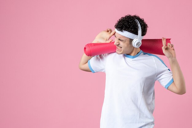 Vue de face crier jeune homme en vêtements de sport avec tapis de yoga