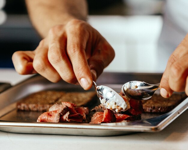 Une vue de face cuisinier préparation de la viande couvrant le repas à l'intérieur de la plaque à frire de la viande