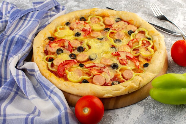 Vue de face d'une délicieuse pizza au fromage avec des saucisses aux olives et des tomates sur le bureau gris