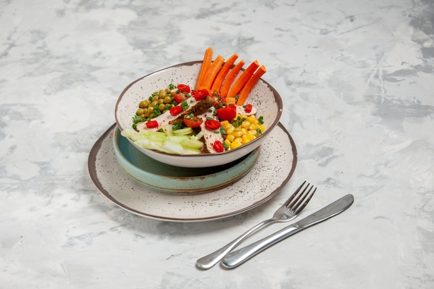 Vue de face d'une délicieuse salade avec divers ingrédients sur une assiette sur des plateaux et des couverts sur une surface blanche avec un espace libre