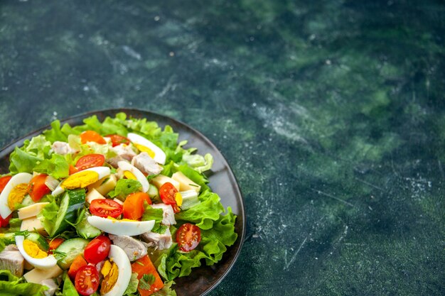 Vue de face de la délicieuse salade faite maison avec de nombreux ingrédients dans une assiette sur le côté droit sur fond de couleurs de mélange vert noir avec espace libre