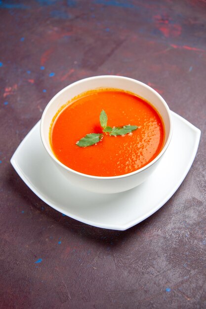 Vue de face délicieuse soupe aux tomates plat savoureux avec une seule feuille à l'intérieur de la plaque sur un espace sombre