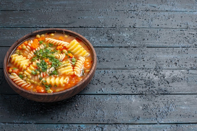 Vue de face délicieuse soupe de pâtes à partir de pâtes italiennes en spirale avec des verts sur le plat de bureau sombre soupe de sauce aux pâtes italiennes dîner