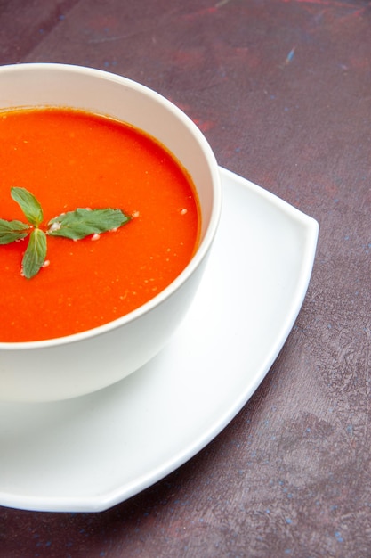 Vue de face délicieuse soupe de tomate plat savoureux avec une seule feuille à l'intérieur de la plaque sur un plat de bureau sombre sauce tomate couleur soupe