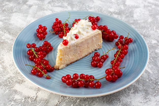 Photo gratuite vue de face de la délicieuse tranche de gâteau à l'intérieur de la plaque ronde bleue avec crème et canneberges rouges sur le bureau gris