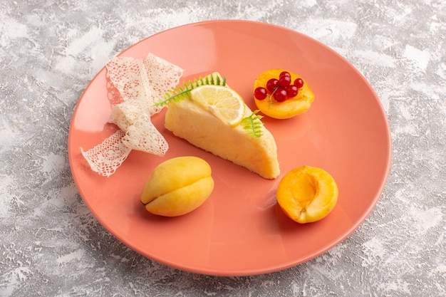 Vue de face d'une délicieuse tranche de gâteau avec morceau de citron et abricots frais sur la surface lumineuse