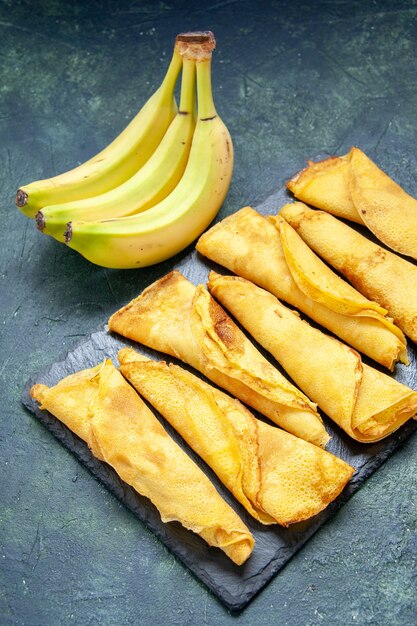 Vue de face de délicieuses crêpes roulées avec des bananes sur une surface sombre