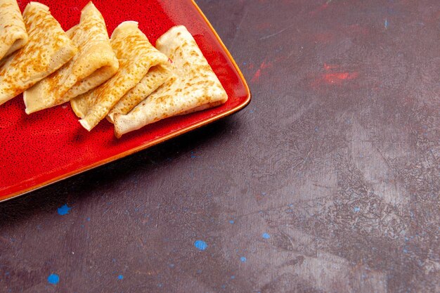 Vue de face de délicieuses crêpes sucrées à l'intérieur d'une assiette rouge sur un espace sombre