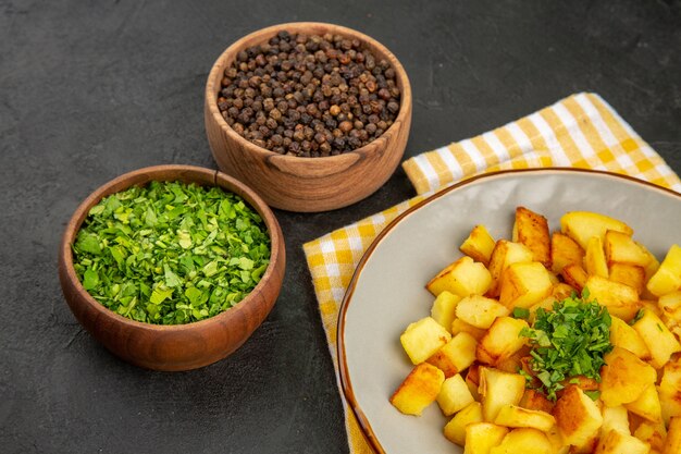 Vue de face de délicieuses pommes de terre frites à l'intérieur de la plaque avec des assaisonnements sur la table sombre