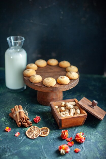 Vue de face de délicieux biscuits sucrés avec du lait et des noix sur la surface bleu foncé