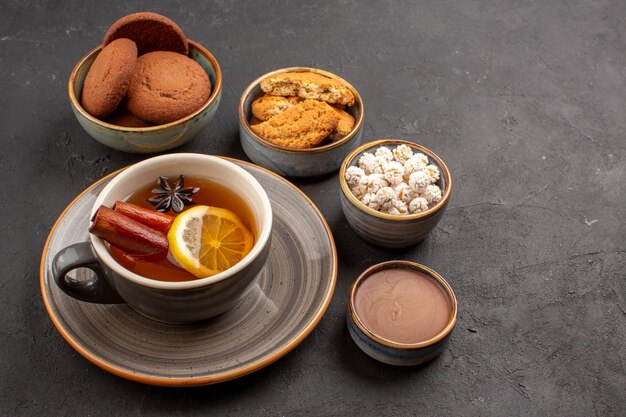 Vue de face de délicieux biscuits avec une tasse de thé sur fond sombre biscuit au sucre dessert biscuit sucré