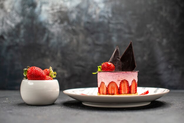 Vue de face délicieux cheesecake à la fraise et au chocolat sur une assiette ovale bol de fraises sur noir