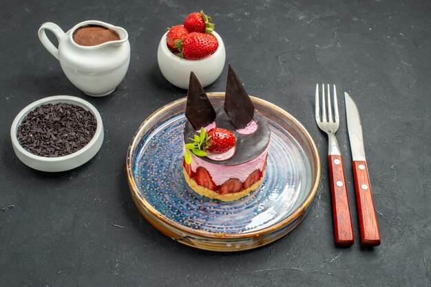 Vue de face délicieux cheesecake à la fraise et au chocolat sur des bols en assiette avec des fraises chocolat noir fourchette et couteau sur fond sombre isolé