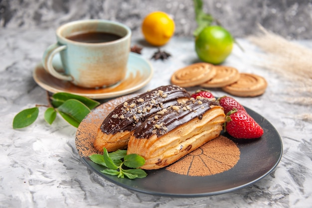 Vue de face de délicieux éclairs au chocolat avec du thé sur un gâteau de dessert aux biscuits de table blanche