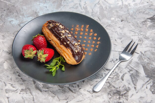 Vue de face de délicieux éclairs au chocolat avec des fraises sur des bonbons de dessert au gâteau de table léger