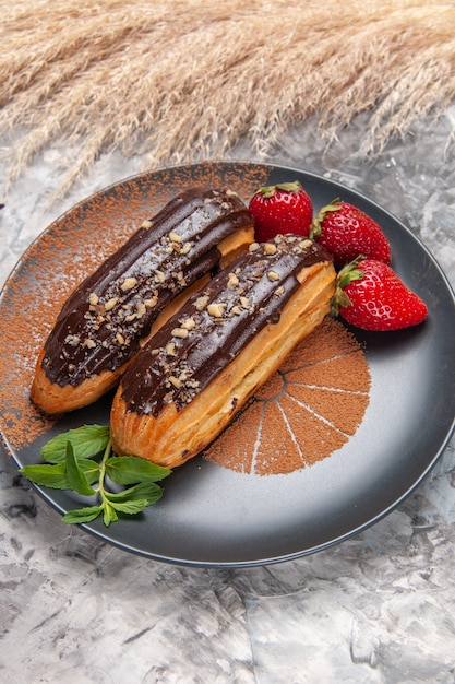 Photo gratuite vue de face de délicieux éclairs au chocolat avec des fraises sur un dessert aux biscuits aux biscuits de table lumineuse