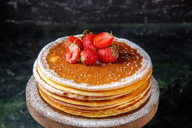 Vue de face délicieux gâteau au miel avec des fraises fraîches sur une planche de bois ronde surface sombre