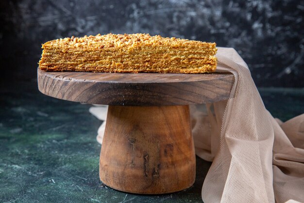 Vue de face de délicieux gâteau au miel tranche de celui-ci sur une surface sombre de planche de bois ronde