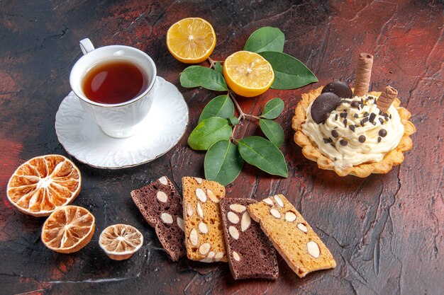 Vue de face délicieux gâteau crémeux avec tasse de thé sur fond sombre