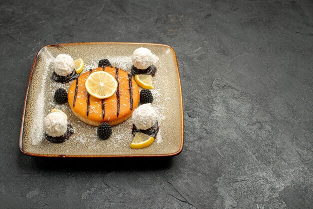 Vue de face délicieux gâteau dessert avec des tranches de citron et des bonbons à la noix de coco sur fond sombre tarte dessert gâteau sucré bonbons thé