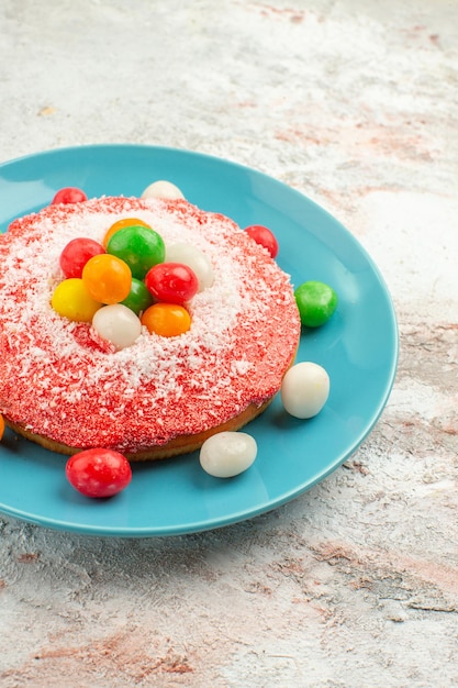 Photo gratuite vue de face délicieux gâteau rose avec des bonbons colorés à l'intérieur de la plaque sur fond blanc tarte gâteau de couleur arc-en-ciel bonbons dessert