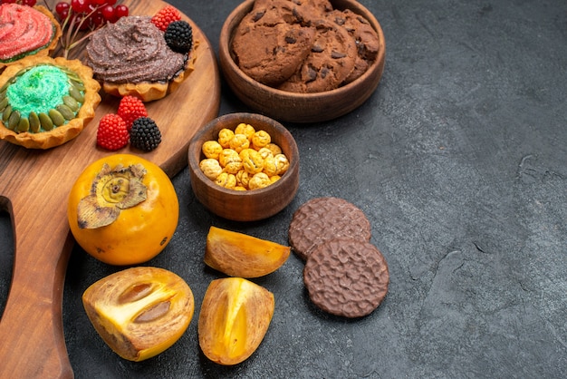 Vue de face de délicieux gâteaux avec des biscuits et des fruits sur fond sombre